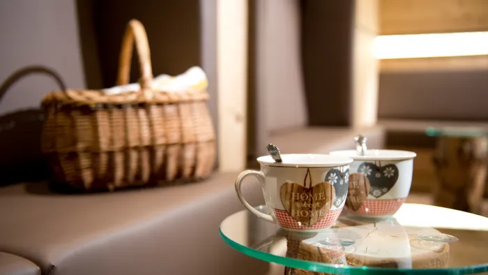 Zwei Keramiktassen mit Herzmotiven und Löffeln auf Glastisch in gemütlicher Lounge mit Picknickkorb